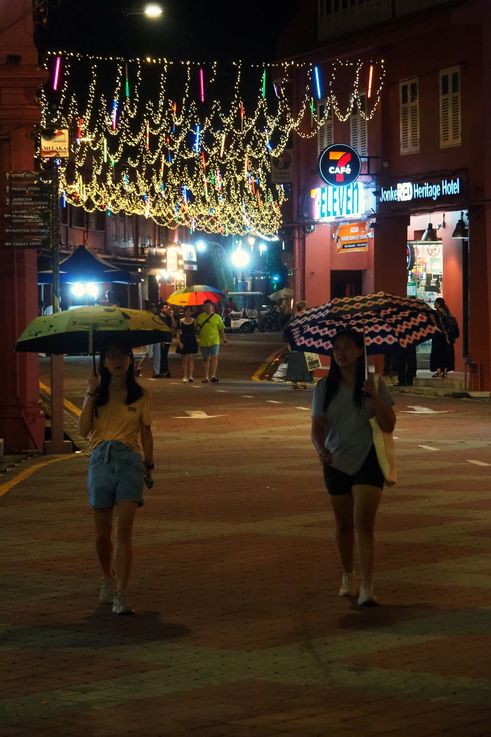 Rue illuminée du Dutch Square de Melaka, la nuit, avec des parapluies.